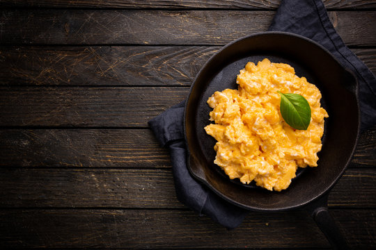 Fresh cooked scrambled eggs in a cast iron skillet on dark wooden background, top view