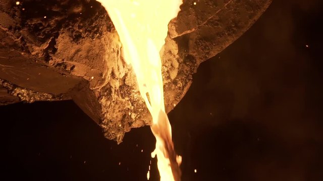 Stream of molten metal poured from one ladle to another in foundry. Liquid metal in metal furnace. Liquid metal production process. Molding molten metal at industrial plant. Slow motion