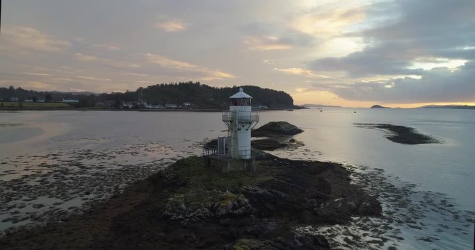 Birds fly around lighthouse lit by dramatic sunset in Scotland, UK