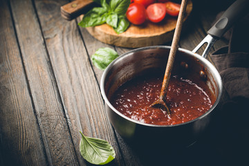 Classic homemade Italian tomato sauce with basil for pasta and pizza in the pan on wooden background.