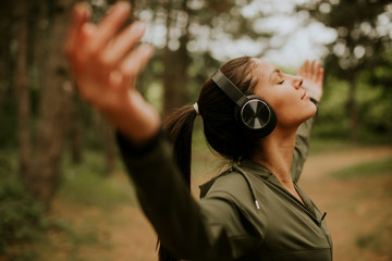 Young woman with earphones preading her arms in the forest because she enjoys training outside