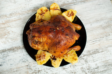 fried chicken with potatoes on a black plate on a white wooden background