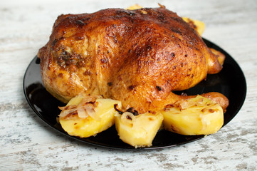 fried chicken with potatoes on a black plate on a white wooden background