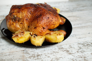 fried chicken with potatoes on a black plate on a white wooden background