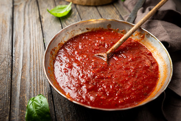 Classic homemade Italian tomato sauce with basil for pasta and pizza in the pan on wooden background.