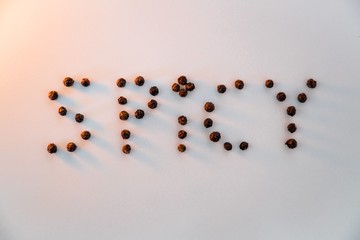 Black pepper balls on a white surface lightened with fire light and creating the word "SPICY"