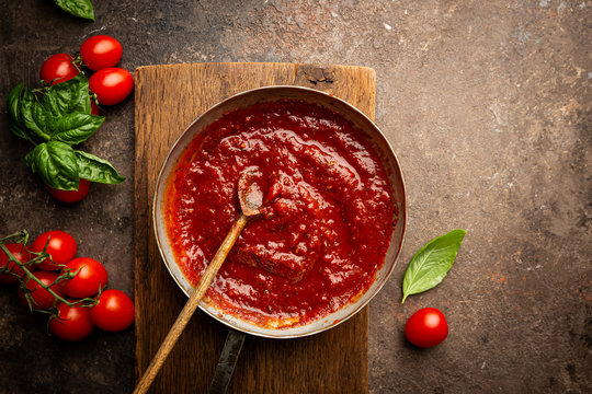 Classic homemade Italian tomato sauce with basil for pasta and pizza in the pan on a wooden chopping board on brown background, top view.