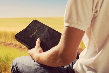 Man reading old Bible book on nature background