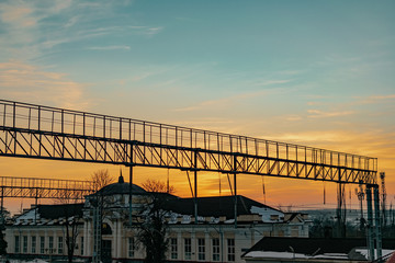 High and narrow bridge at the railway station. For crossing over tracks and trains. A long bridge with steps in the evening at sunset.
