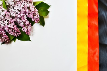 Happy German Unity Day, October 3. German national flag made of ribbons and a bouquet of lilacs isolated on a white background. Place for text. The concept of a holiday, unity.