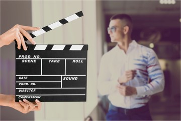 Hands holding film clapper board with an actor on background