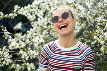 Smiling woman in sunglasses on background of blossoming apple tree