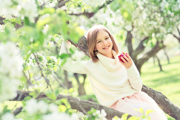 Beautiful teenage girl having fun in bluming garden with blossom flowers, ready to eat red delicious apple