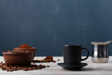 Obraz na płótnie Canvas Espresso cup, roasted Arabica beans in clay bowls, coffee powder, metal Turkish pot on while table against dark blue wall. Side view, copy space. Coffee shop, morning, baristas workplace concept
