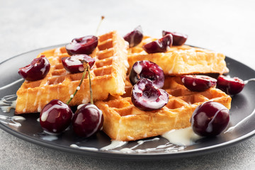 Belgian fluted waffles with fresh cherries and cream on a plate. Soft homemade waffles, sweet dessert with cherries.