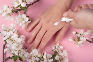 beauty skin care, girl smears cream on her hands on flower pink background.