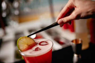 The barman decorates the alcoholic cocktail with a slice of  citrus using the pliers.  view from the back