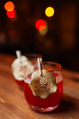 red alcoholic cocktail decorated with dried pear slice on a wooden table in a bar. Blurry lights in the background
