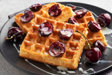 Belgian fluted waffles with fresh cherries and cream on a plate. Soft homemade waffles, sweet dessert with cherries.