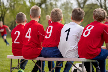 Team Sports Background. Boys in a Sport Team Sitting Together on a Bench. Kids Wearing Red Soccer Jersey Shirts with Numbers on Back. School Level Football Team Playing Match