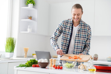Portrait of positive cheerful gourmet guy enjoy proper nutrition weekend cook fresh salad add sliced tomato wear casual checkered plaid shirt in kitchen house indoors