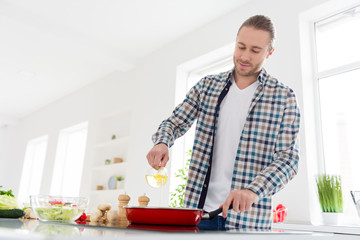 Photo of positive handsome man cook tasty delicious supper meal pouring sunflower oil on frying pan wear casual checkered plaid shirt stand in kitchen house