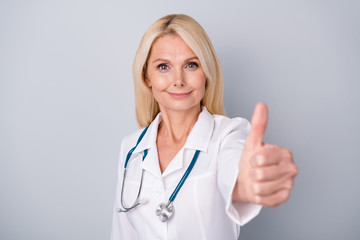 Positive experienced retired pensioner woman infection specialist show thumb sign approve quality of corona virus medication treatment therapy wear white coat isolated gray color background