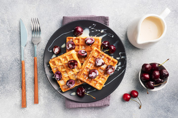 Belgian fluted waffles with fresh cherries and cream on a plate. Soft homemade waffles, sweet dessert with cherries.