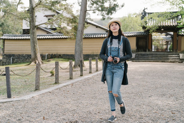 pleasant female tourist hiking on gravel path is admiring the beauty of the japanese style garden. korean lady looking into distance is visiting an ancient site with pine trees.