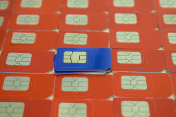 Several blue SIM cards for mobile communications are located among many red cards. Technological...