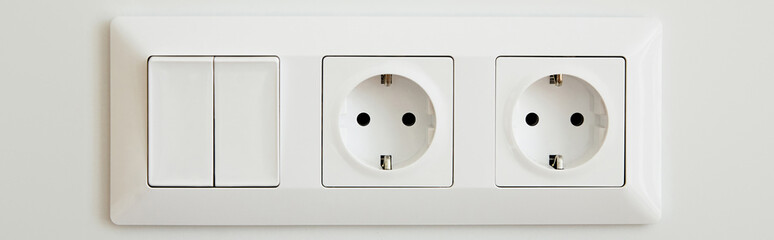 panoramic crop of power sockets near switch on white wall