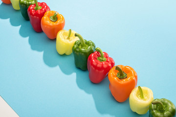 fresh colorful bell peppers in row on blue surface