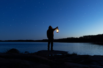Man holding the old lamp outdoors near the lake. Hand holds a large lamp in the dark. Ancient...