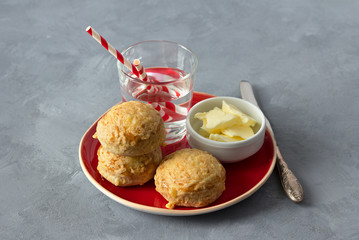 Homemade freshly baked scones with cheese and herbs on a red plate with butter on a gray textured background. Traditional english buns