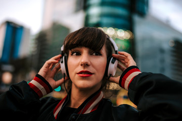 Beautiful spanish woman listening to music with earphones and smart phone outdoors in the night city