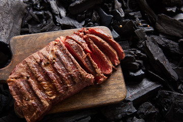 top view of cut fresh grilled tasty steak with rare roasting on wooden cutting board on black coals