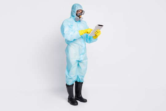 Full length photo of focused doctor man use tablet search covid19 information statistics wear white yellow suit hazmat breathing mask isolated over gray color background