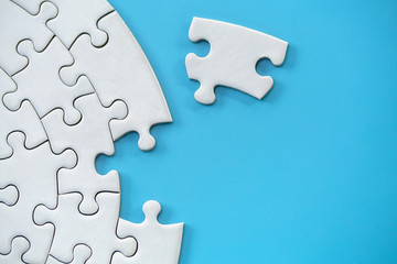 Unfinished white jigsaw puzzle on blue background with copy space. Business strategy teamwork and...