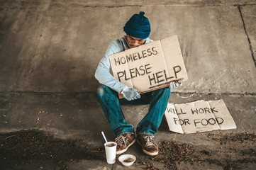 The beggars sit under the bridge with a homeless message. Please help.