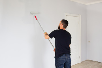 A man paints a wall in an apartment with a roller. Repair in the apartment.