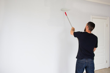 A man paints a wall in an apartment with a roller. Repair in the apartment.
