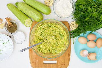step-by-step recipe to cook pancakes of zucchini and greens on a light background. with the addition of eggs, flour, garlic, pepper. mix the ingredients in a bowl. the view from the top