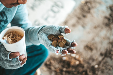 Begging under the bridge with a cup containing coins and instant noodles