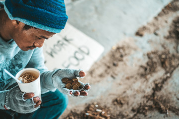 Begging under the bridge with a cup containing coins and instant noodles
