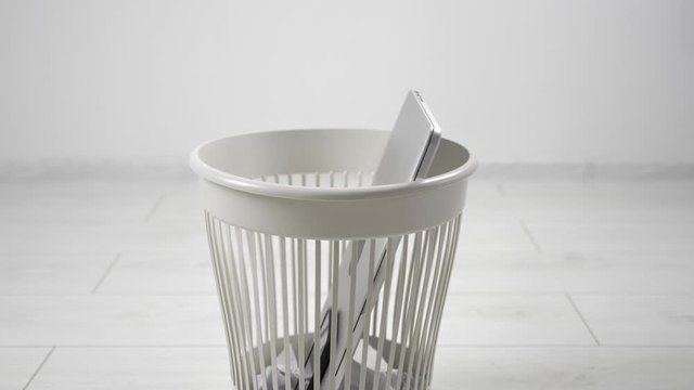 Close-up throwing laptop and smartphone to the trash bin. The concept of getting rid of gadgets and electronics.