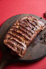 tasty grilled steak served on wooden boards on red background with pepper