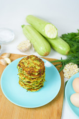 veggie fried pancakes with zucchini and greens on a blue plate on a light background on a wooden Board . recipe with the addition of eggs and flour. top view, selective focus, space for text