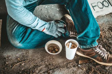 Begging under the bridge with a cup containing coins and instant noodles