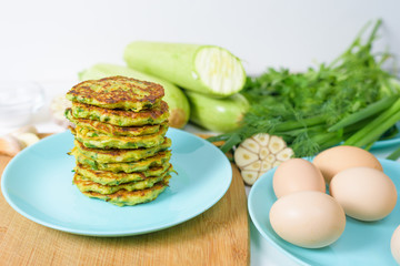 veggie fried pancakes with zucchini and greens on a blue plate on a light background on a wooden Board . recipe with the addition of eggs and flour. top view, selective focus, space for text