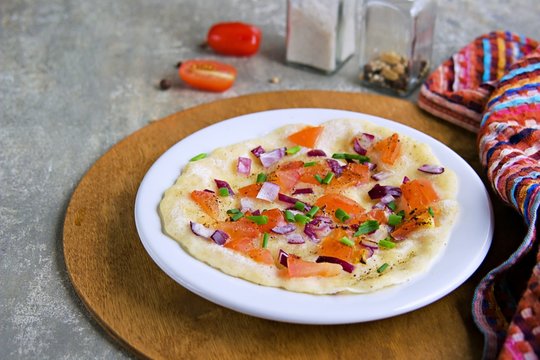 Uttapam, Indian semolina pancake with tomato and purple onion on a white plate on a gray concrete background. Indian food, breakfast.
